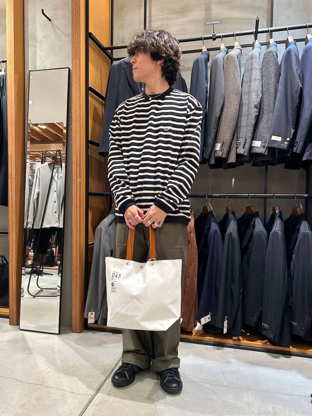 ホワイト系のトートバッグ、ブラック系のTシャツ/カットソー、グリーン系のチノパンツを着用したメンズの秋コーディネートの2枚目の写真