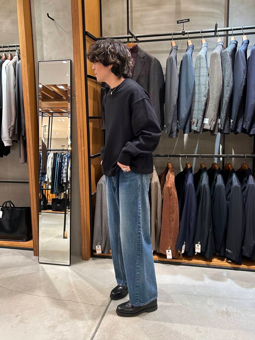 ブラック系のニット/セーター、ブラック系のトートバッグ、ブルー系のデニムパンツを着用したメンズの秋コーディネートの2枚目の写真