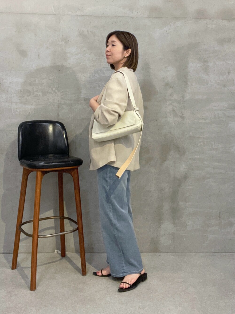 ブルー系のデニムパンツ、ベージュ系のテーラードジャケット、ホワイト系のショルダーバッグを着用したレディースの夏コーディネートの4枚目の写真