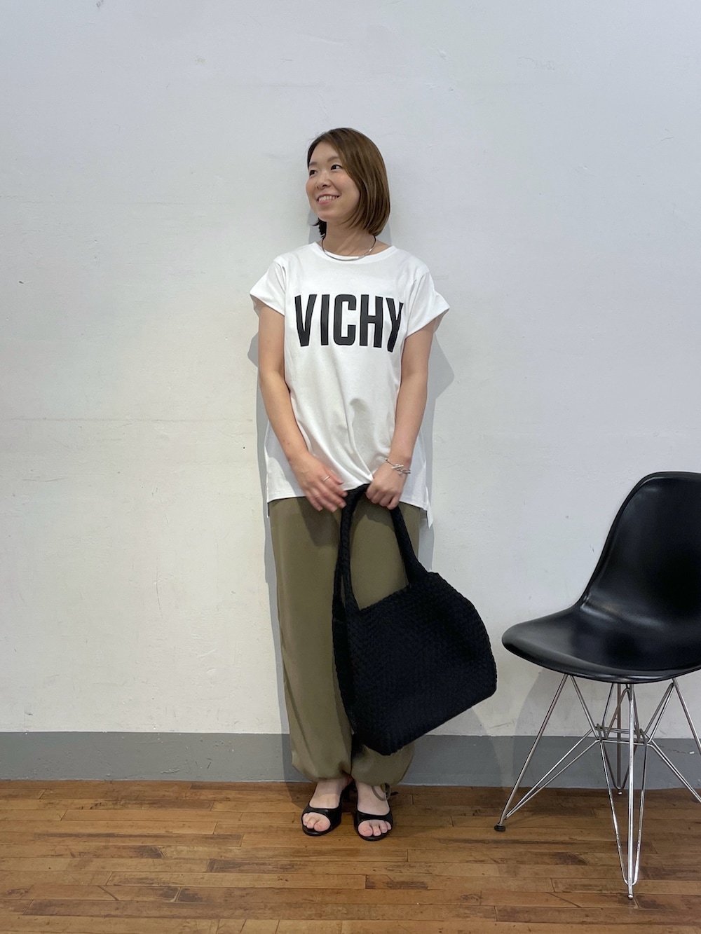 ブラック系のトートバッグ、ホワイト系のTシャツ/カットソー、グリーン系のスラックスを着用したレディースの夏コーディネートの4枚目の写真