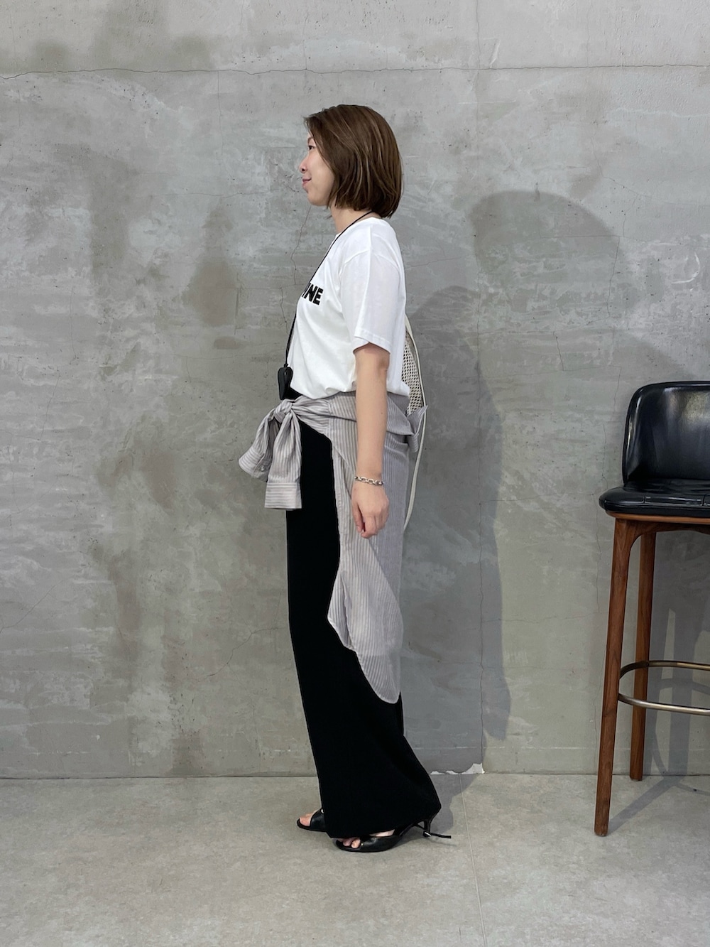 ブラック系のスラックス、ホワイト系のショルダーバッグ、ホワイト系のTシャツ/カットソーを着用したレディースの夏コーディネートの2枚目の写真