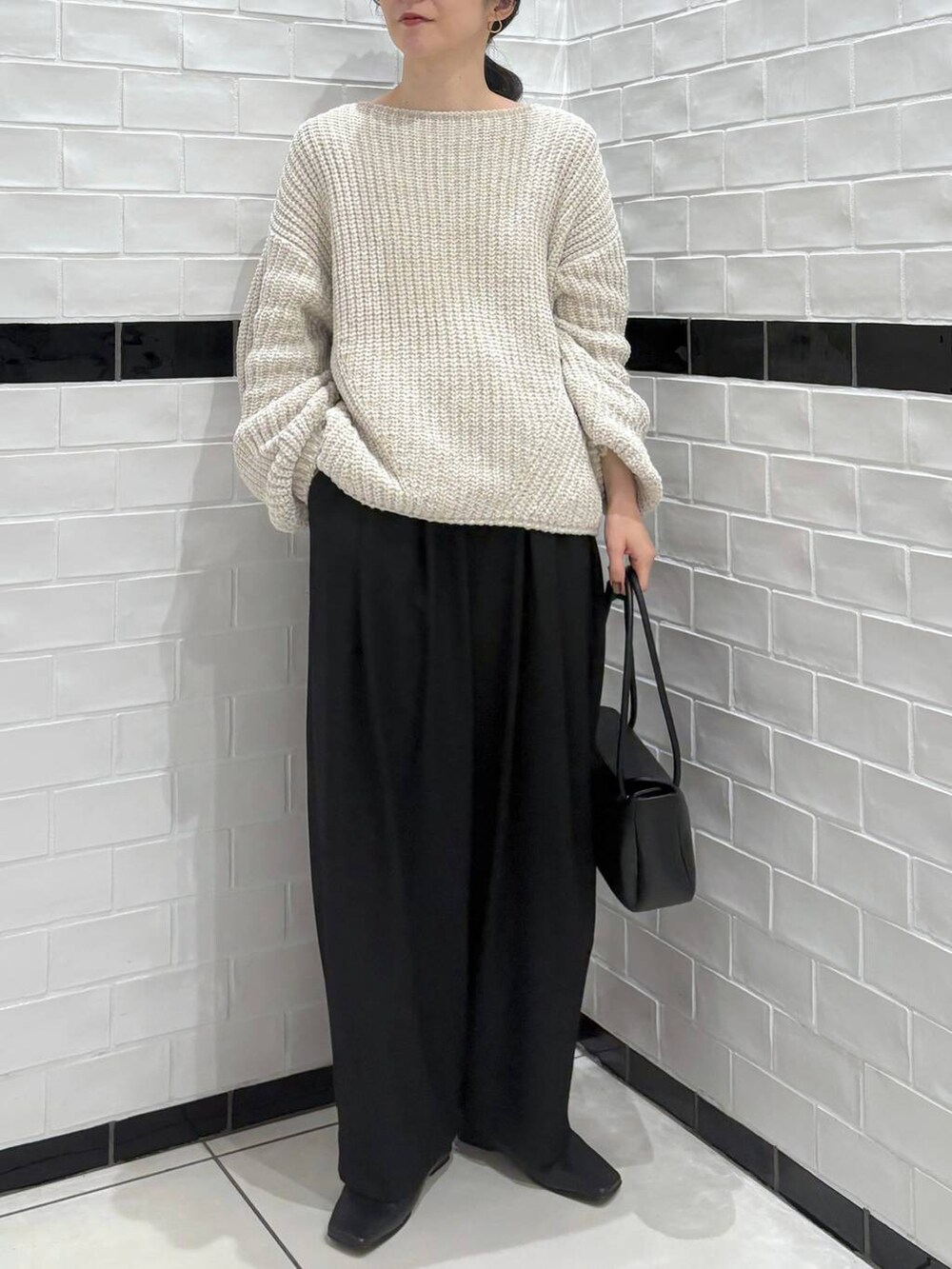 ブラック系のスラックス、ベージュ系のニット/セーター、ブラック系のショルダーバッグを着用したレディースの冬コーディネートの2枚目の写真