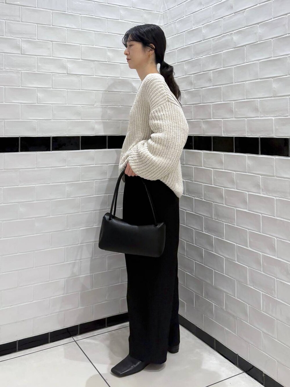 ブラック系のスラックス、ベージュ系のニット/セーター、ブラック系のショルダーバッグを着用したレディースの冬コーディネートの3枚目の写真