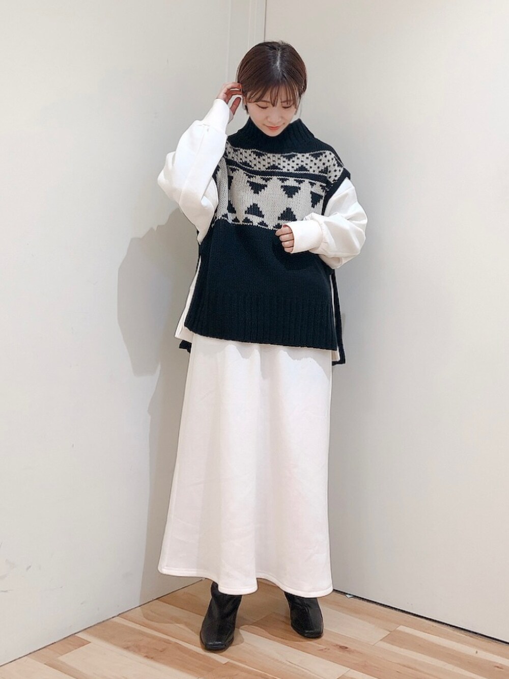 ブラック系のブーツ、ホワイト系のスカート、ブラック系のベストを着用したレディースの秋コーディネートの2枚目の写真