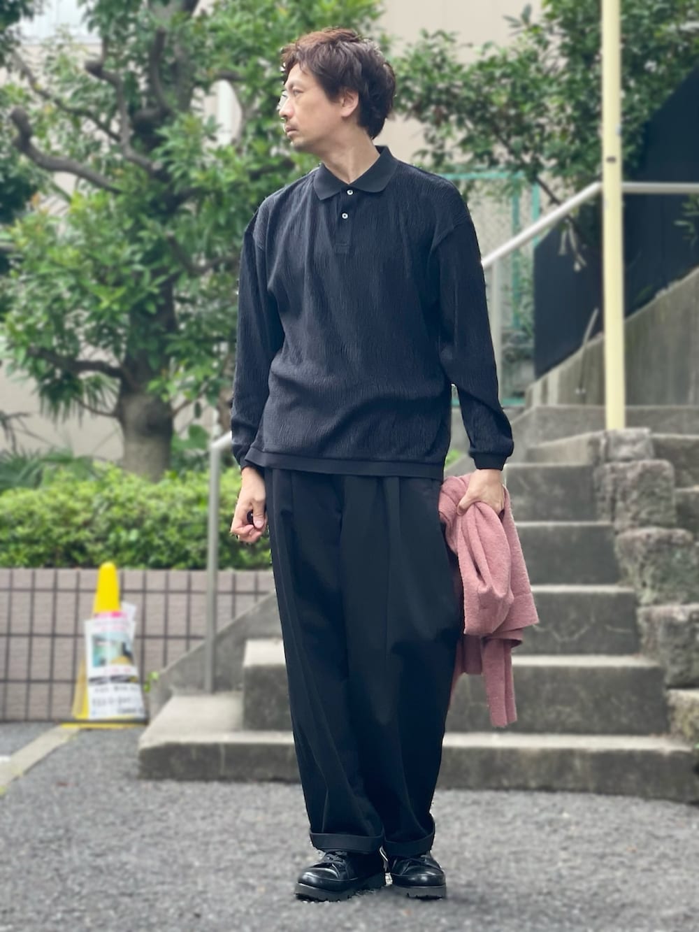 ブラック系のポロシャツ、ピンク系のカーディガン/ボレロ、ブラック系のチノパンツを着用したメンズの秋コーディネートの2枚目の写真