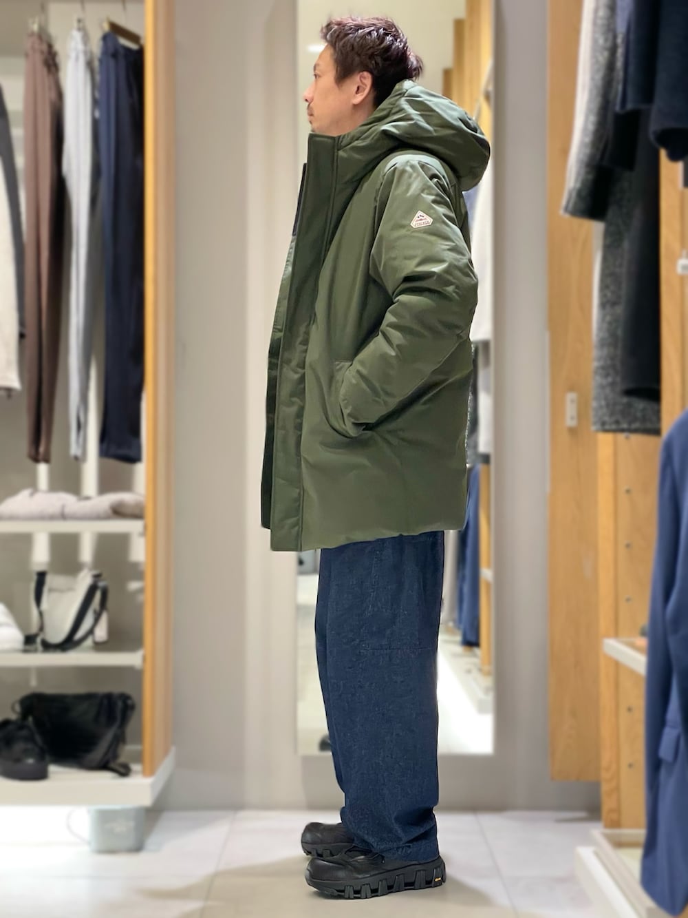 ブラック系のカーディガン/ボレロ、グリーン系のダウンジャケット/コート、ブルー系のデニムパンツを着用したメンズの秋コーディネートの2枚目の写真