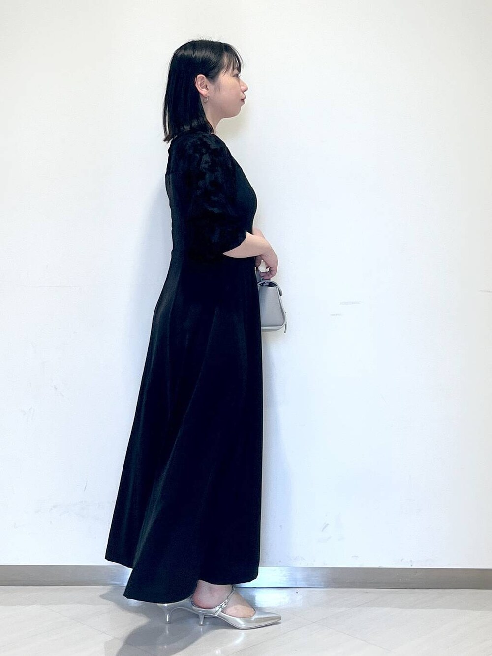 ブラック系のドレス、シルバー系のサンダル、グレー系のショルダーバッグを着用したレディースの春コーディネートの2枚目の写真