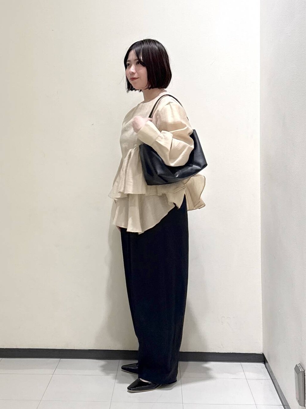 ブラック系のショルダーバッグ、ベージュ系のシャツ/ブラウス、ブラック系のパンプスを着用したレディースの春コーディネートの2枚目の写真