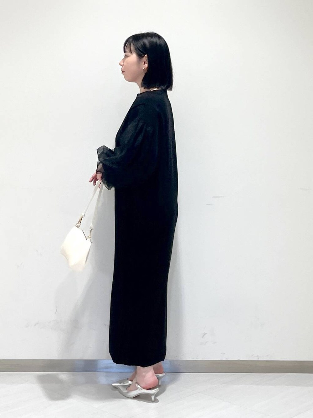 シルバー系のサンダル、ホワイト系のショルダーバッグ、ブラック系のワンピースを着用したレディースの冬コーディネートの2枚目の写真