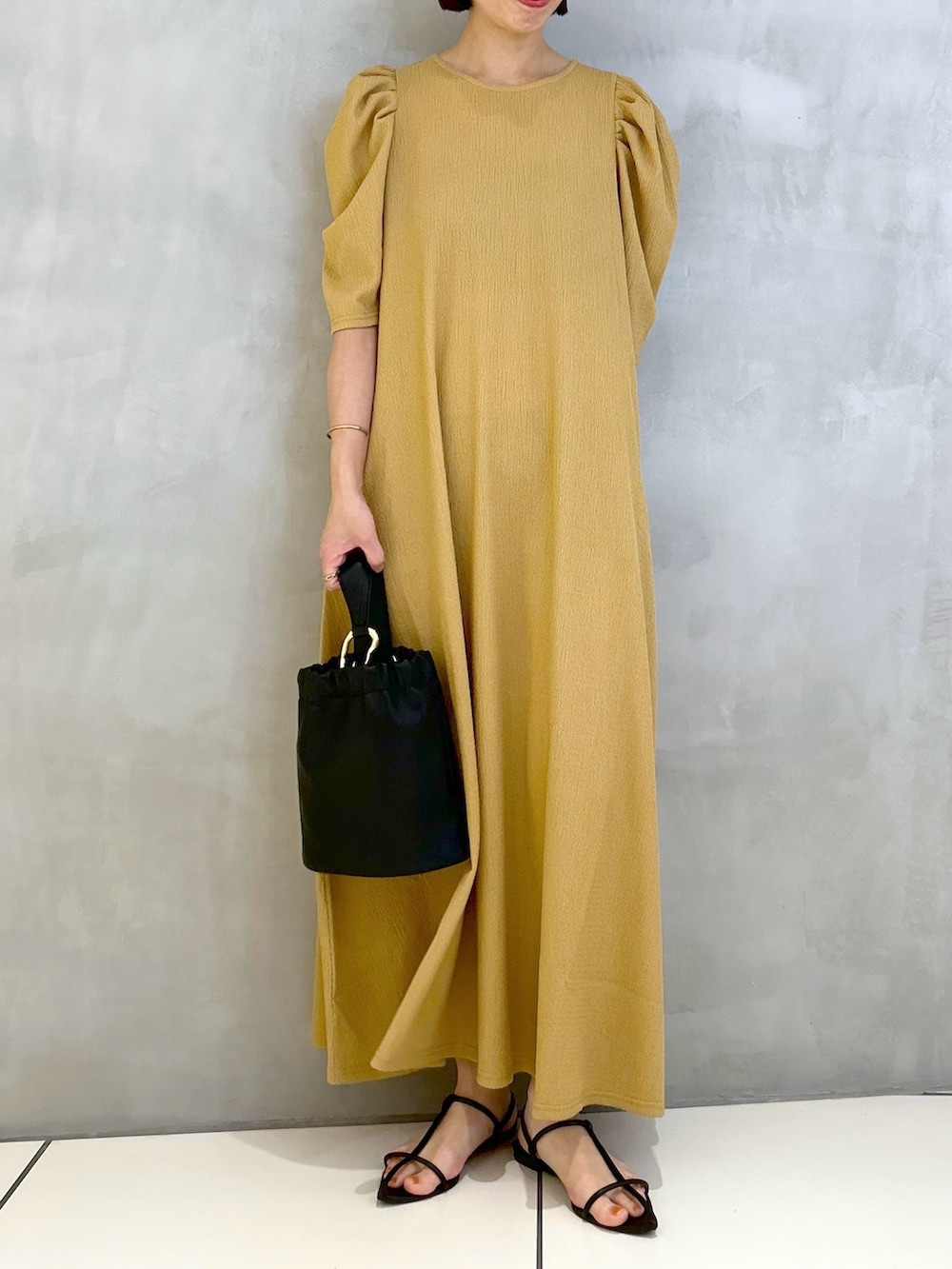 オレンジ系のワンピース、ブラック系のサンダル、ブラック系のショルダーバッグを着用したレディースの春コーディネートの3枚目の写真