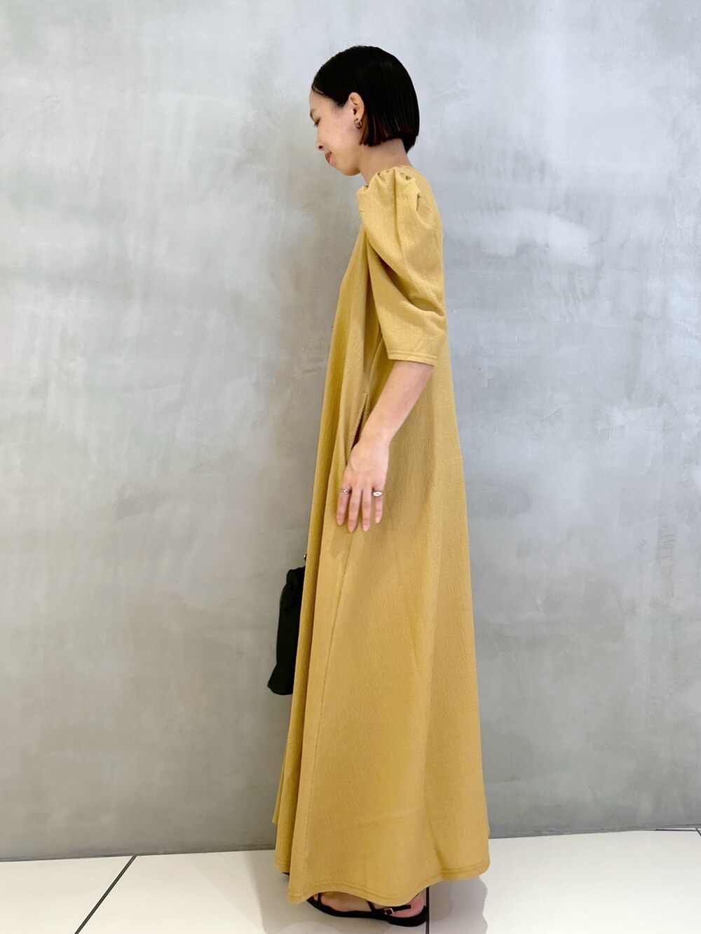 オレンジ系のワンピース、ブラック系のサンダル、ブラック系のショルダーバッグを着用したレディースの春コーディネートの2枚目の写真