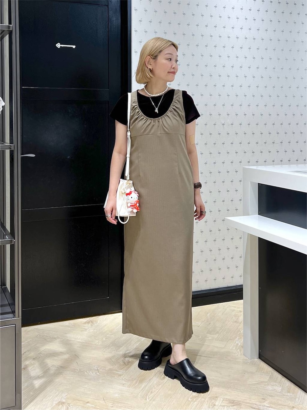 ホワイト系のショルダーバッグ、ブラック系のスリッポン、ベージュ系のワンピースを着用したレディースの夏コーディネートの2枚目の写真