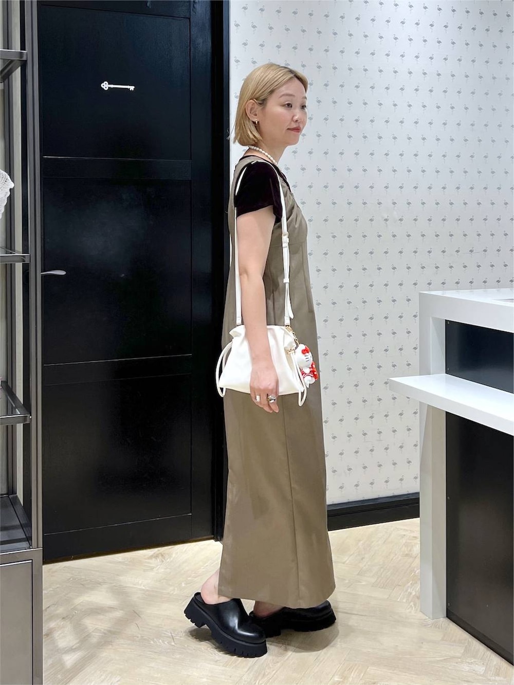 ホワイト系のショルダーバッグ、ブラック系のスリッポン、ベージュ系のワンピースを着用したレディースの夏コーディネートの4枚目の写真