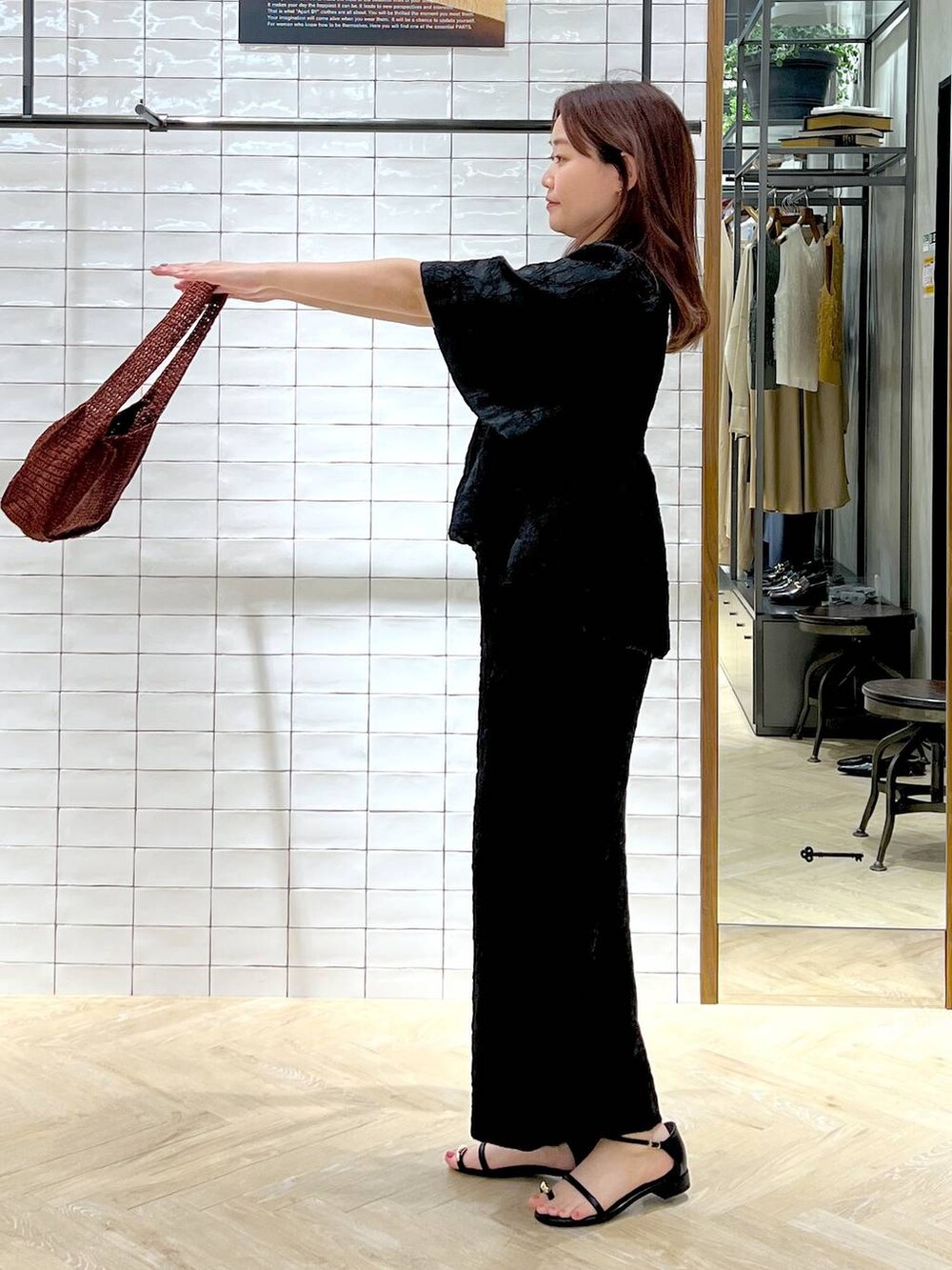 ブラウン系のハンドバッグ、ブラック系のサンダル、ブラック系のワンピースを着用したレディースの夏コーディネートの2枚目の写真