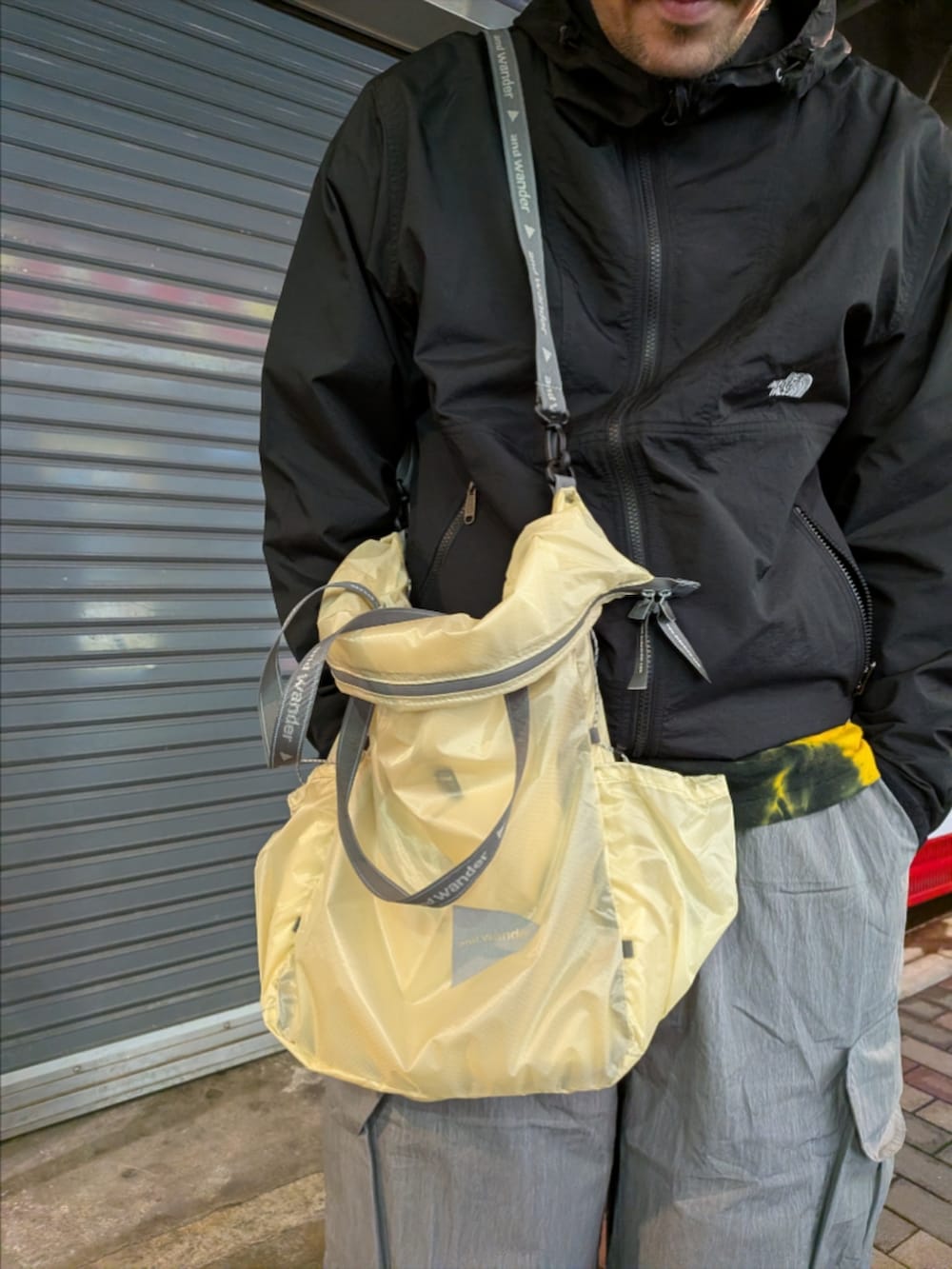 ブラック系のナイロンジャケット、グレー系のカーゴパンツ、ホワイト系のトートバッグを着用したメンズの春コーディネートの3枚目の写真