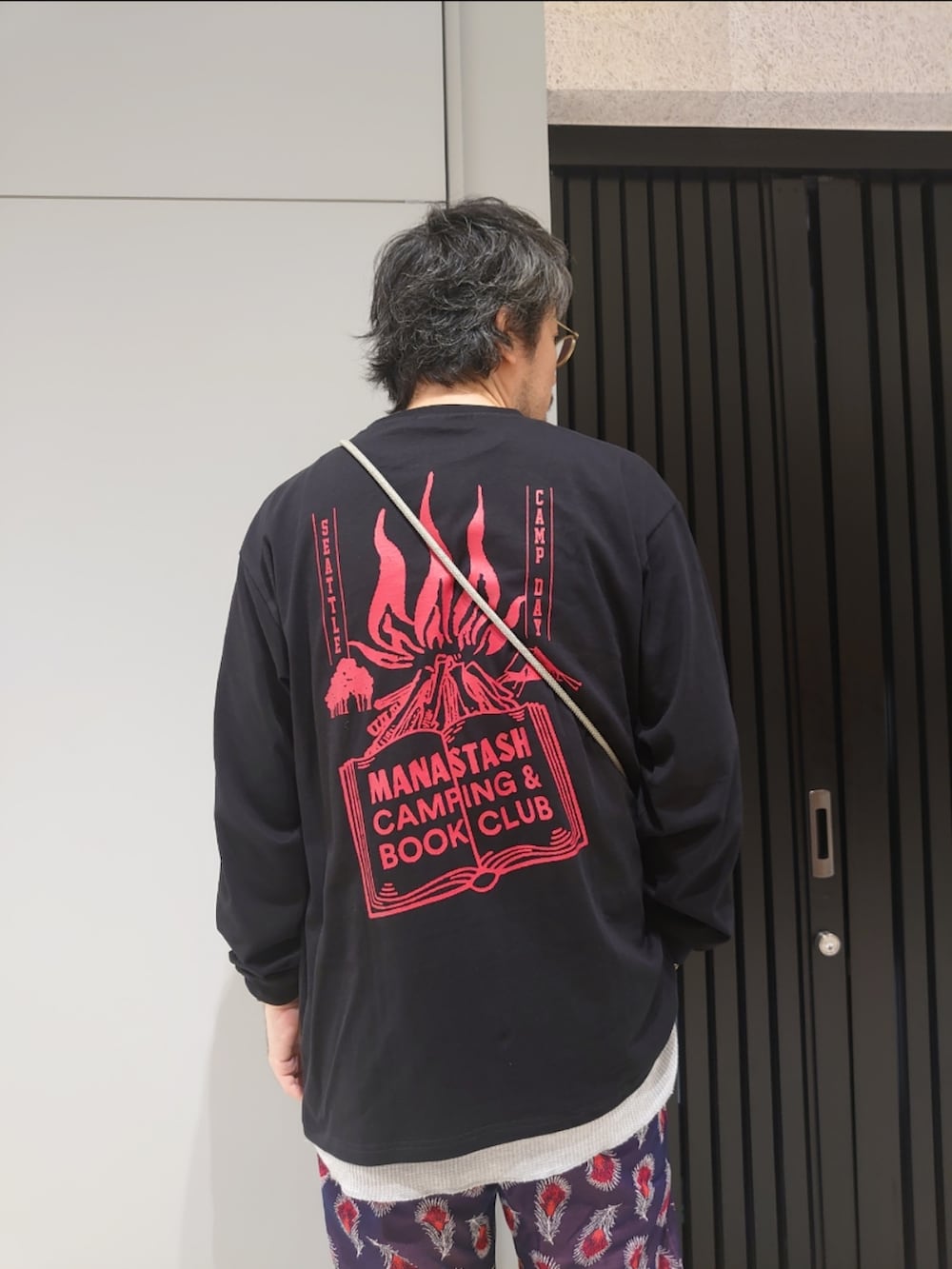 ブラック系のTシャツ/カットソー、ブラック系のショルダーバッグ、グリーン系のスマホグッズを着用したメンズの夏コーディネートの3枚目の写真