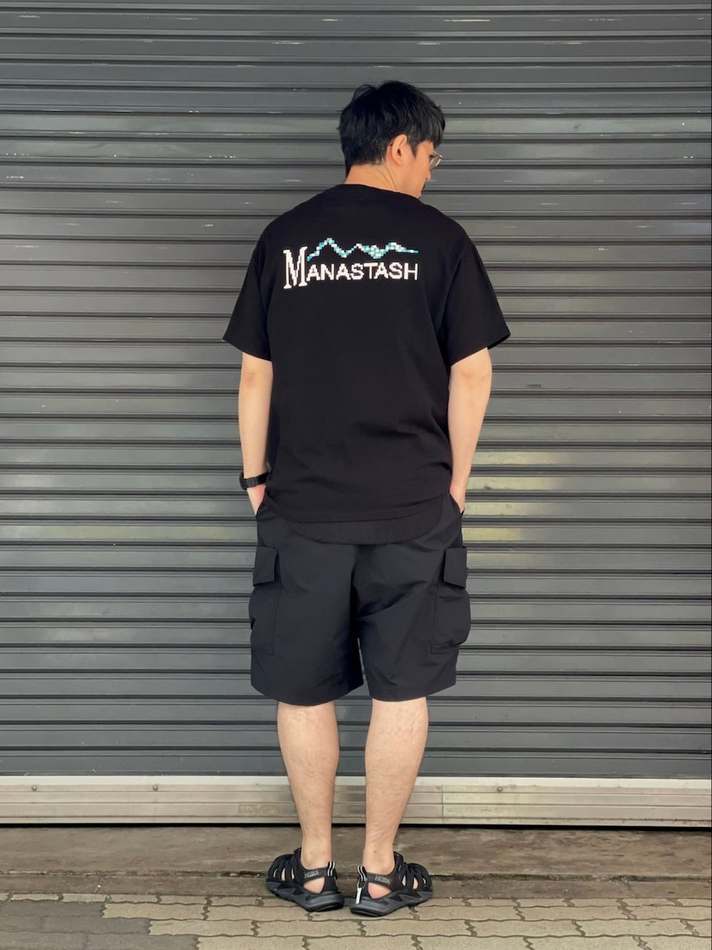 ブラック系のTシャツ/カットソー、ブラック系のカーゴパンツ、ブラック系のサンダルを着用したメンズの春コーディネートの2枚目の写真