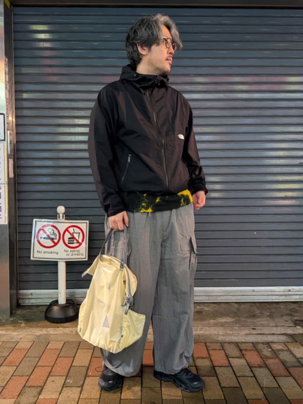 ブラック系のナイロンジャケット、グレー系のカーゴパンツ、ホワイト系のトートバッグを着用したメンズの春コーディネートの2枚目の写真