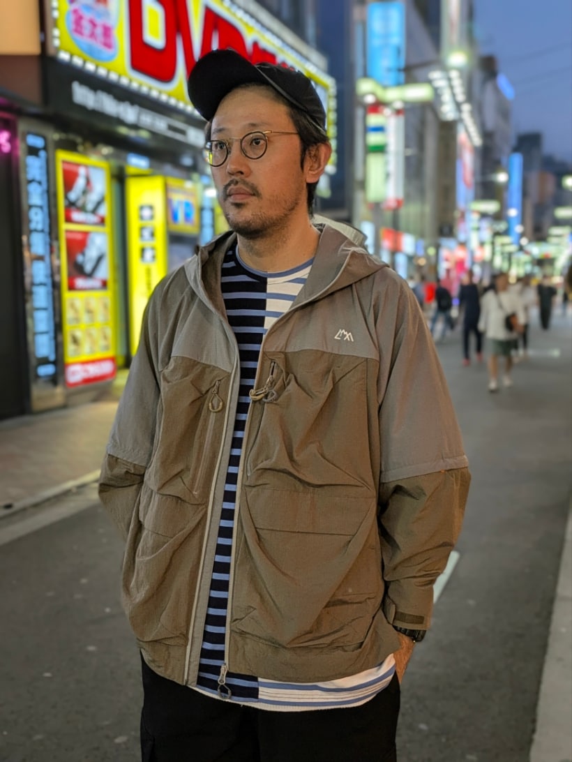 ブルー系のTシャツ/カットソー、ベージュ系のマウンテンパーカー、ブラック系のキャップを着用したメンズの秋コーディネートの3枚目の写真