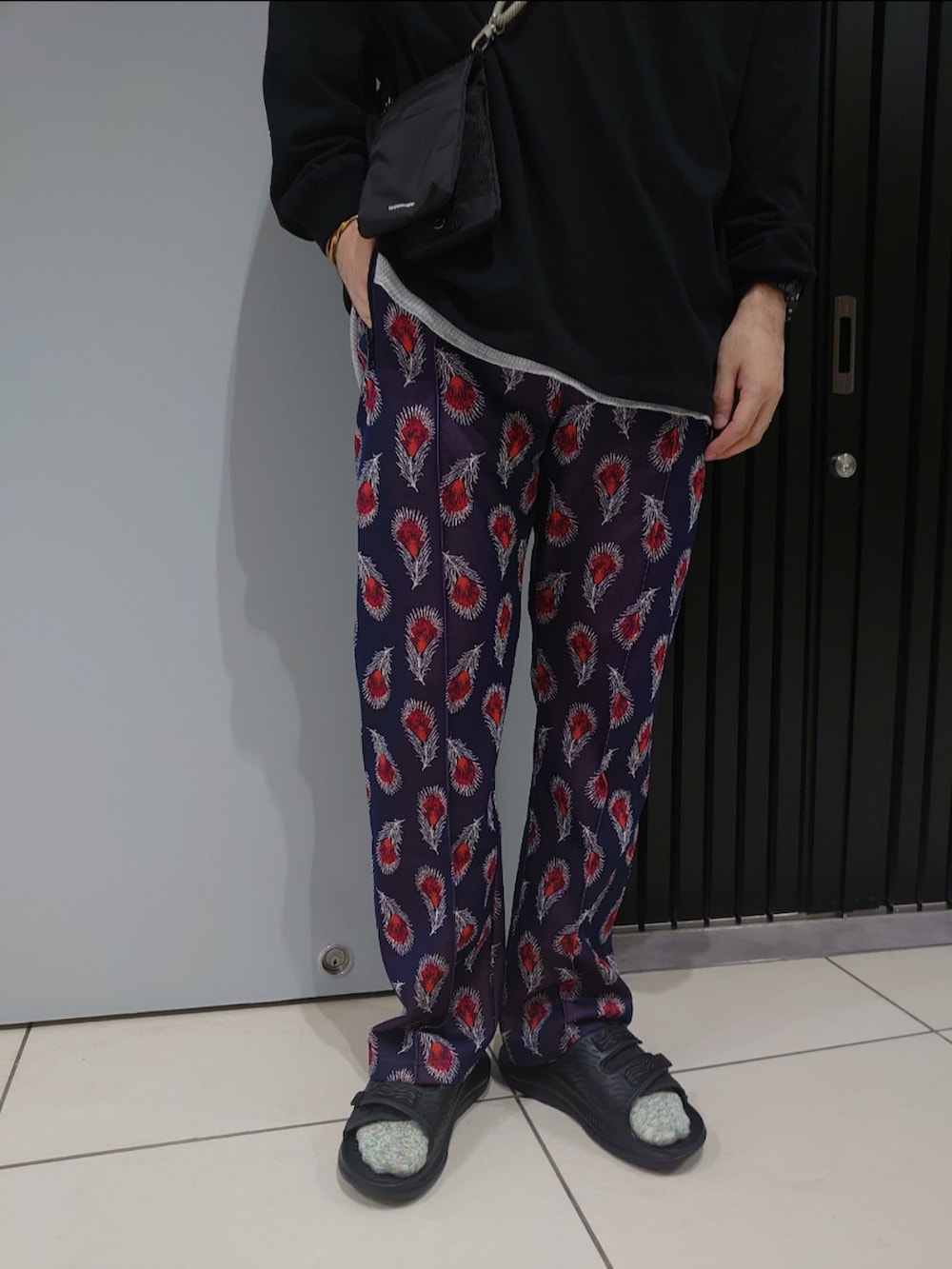 ブラック系のTシャツ/カットソー、ブラック系のショルダーバッグ、グリーン系のスマホグッズを着用したメンズの夏コーディネートの2枚目の写真