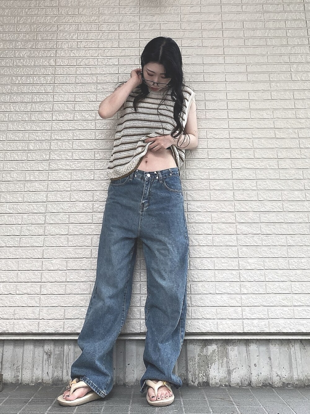 ベージュ系のベスト、ブルー系のデニムパンツ、ベージュ系のサンダルを着用したレディースの夏コーディネートの3枚目の写真