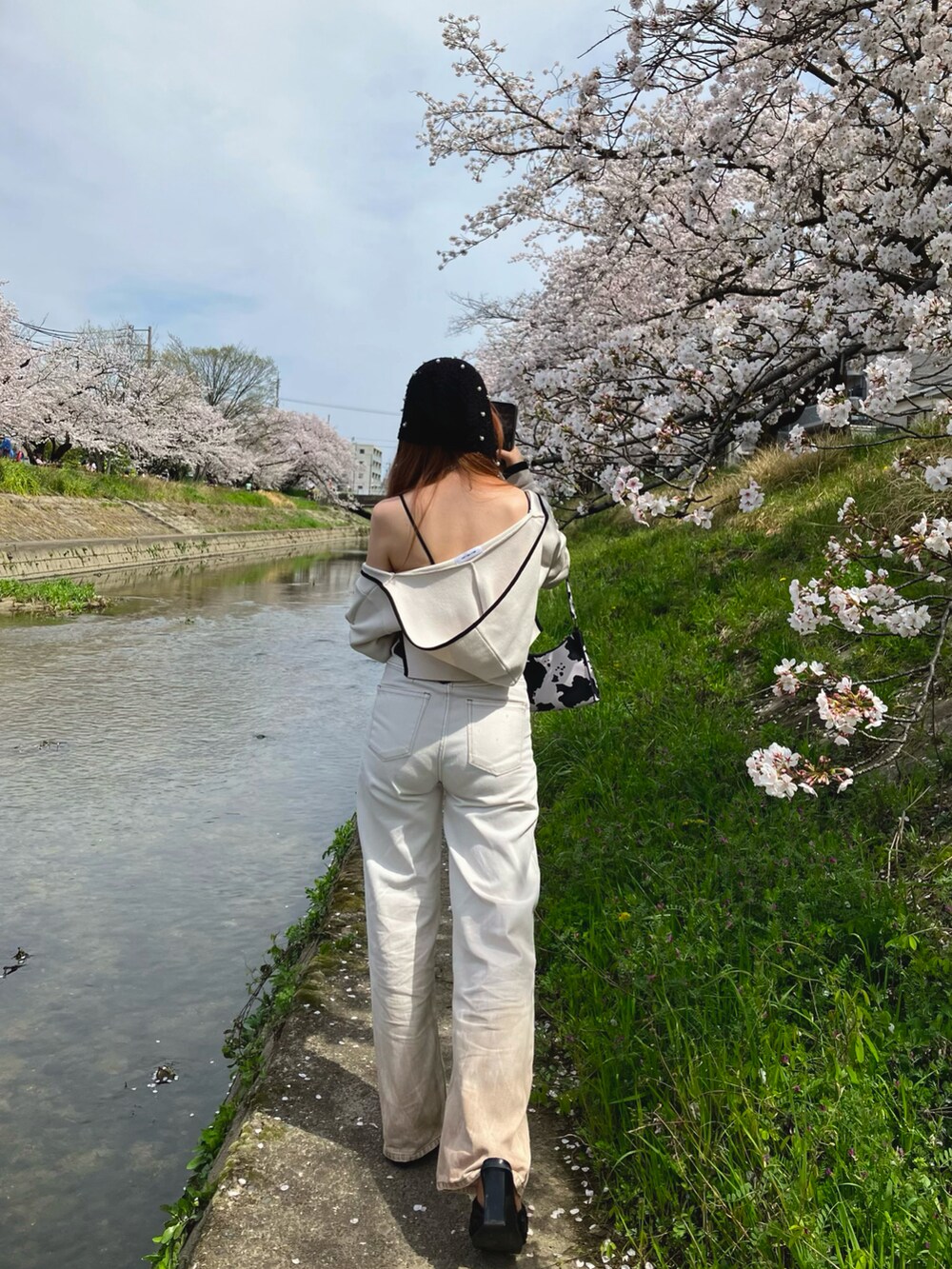 ホワイト系のトップス、ホワイト系のデニムパンツ、ブラック系のサンダルを着用したレディースの春コーディネートの2枚目の写真
