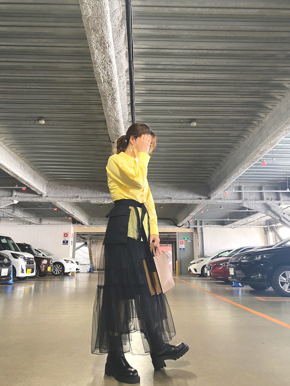 ブラック系のスカート、ブラック系のブーツ、ベージュ系のトートバッグを着用したレディースの春コーディネートの2枚目の写真