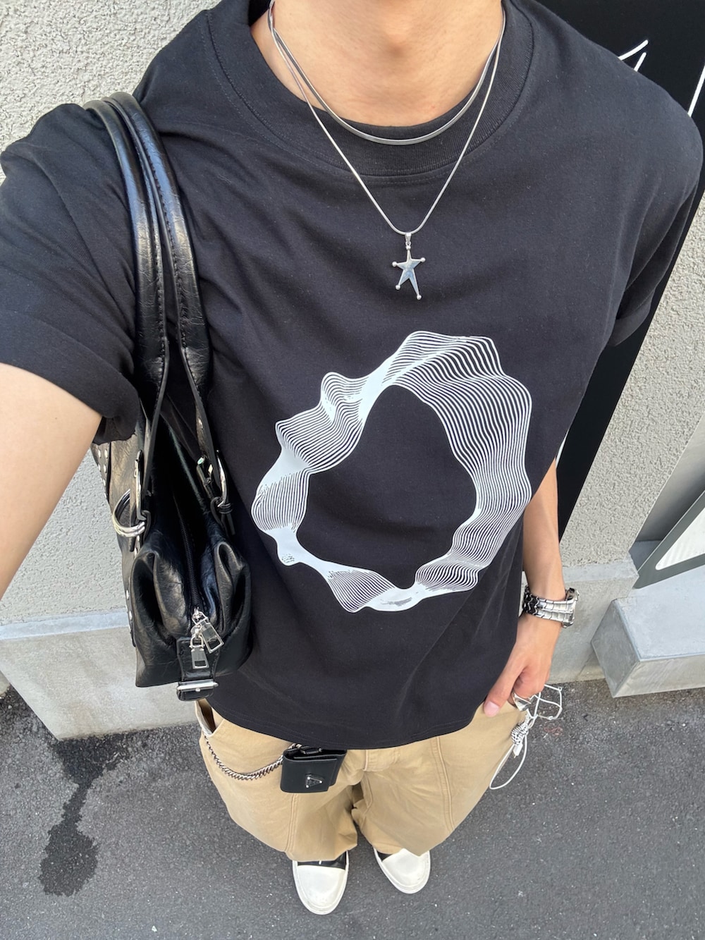 ブラック系のTシャツ/カットソー、ブラック系のショルダーバッグ、ベージュ系のチノパンツを着用したメンズの夏コーディネートの5枚目の写真
