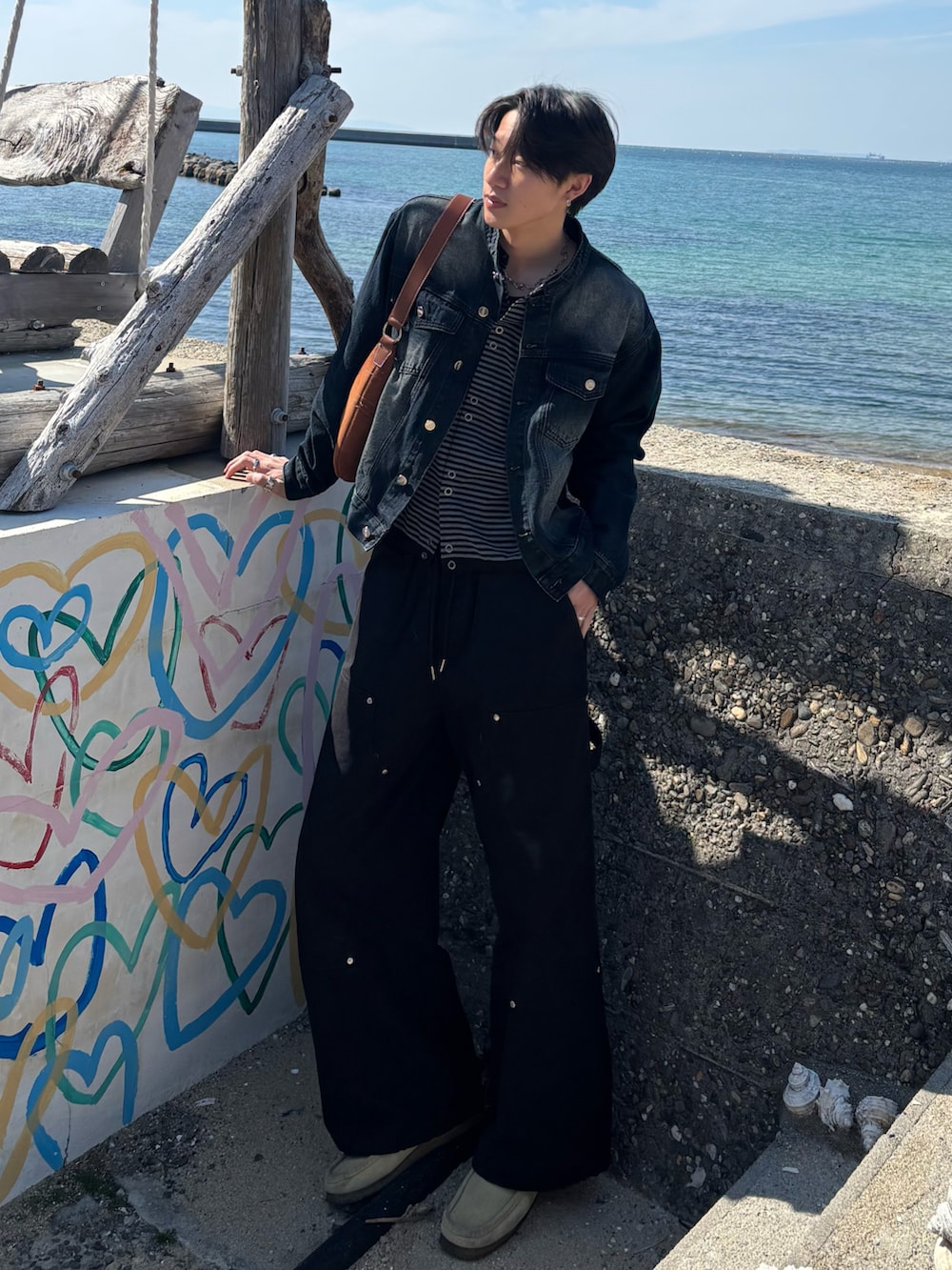 ブルー系のデニムジャケット、ブラック系のカーディガン/ボレロ、ブラウン系のショルダーバッグを着用したメンズの春コーディネートの3枚目の写真