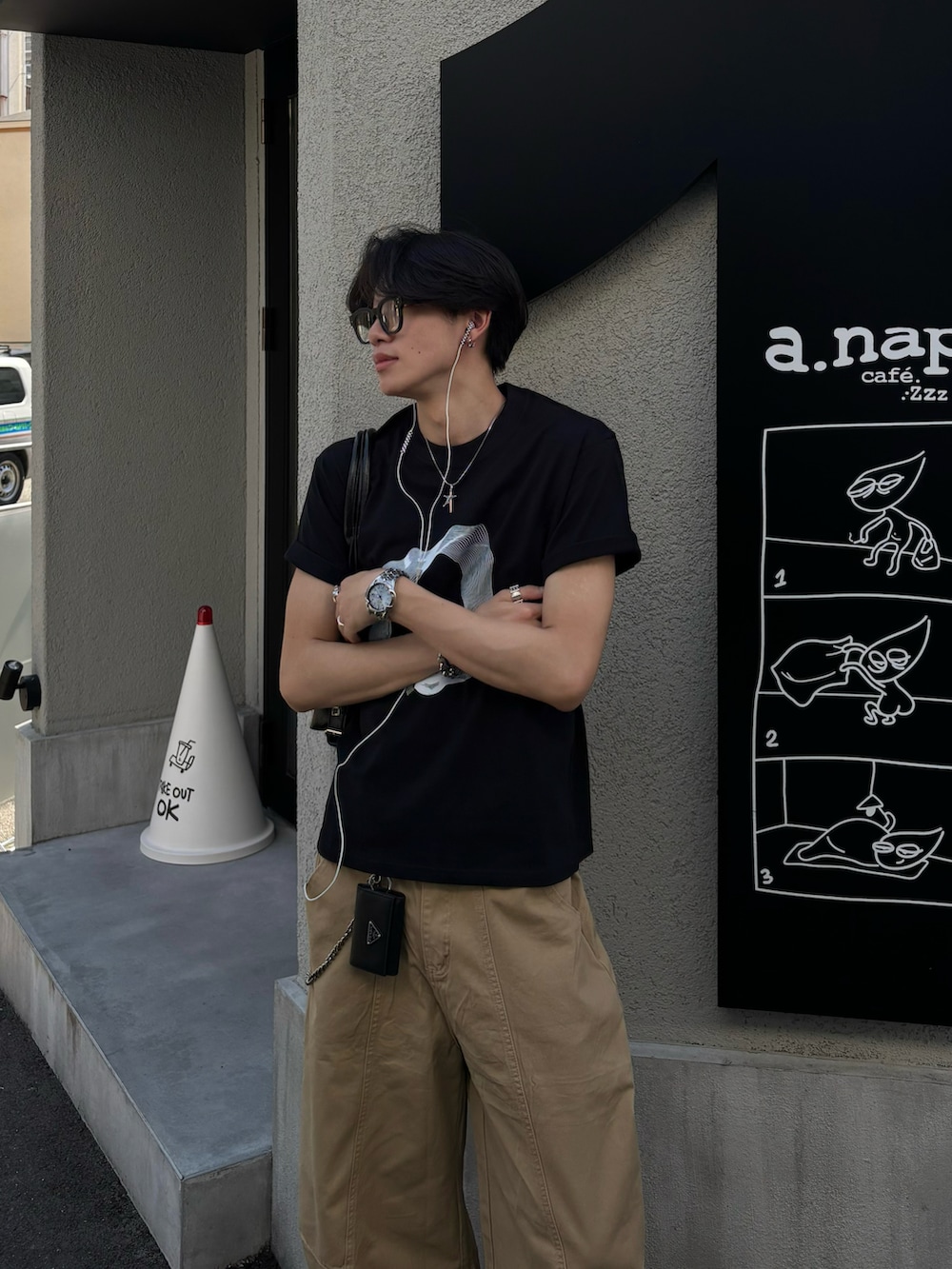 ブラック系のTシャツ/カットソー、ブラック系のショルダーバッグ、ベージュ系のチノパンツを着用したメンズの夏コーディネートの3枚目の写真