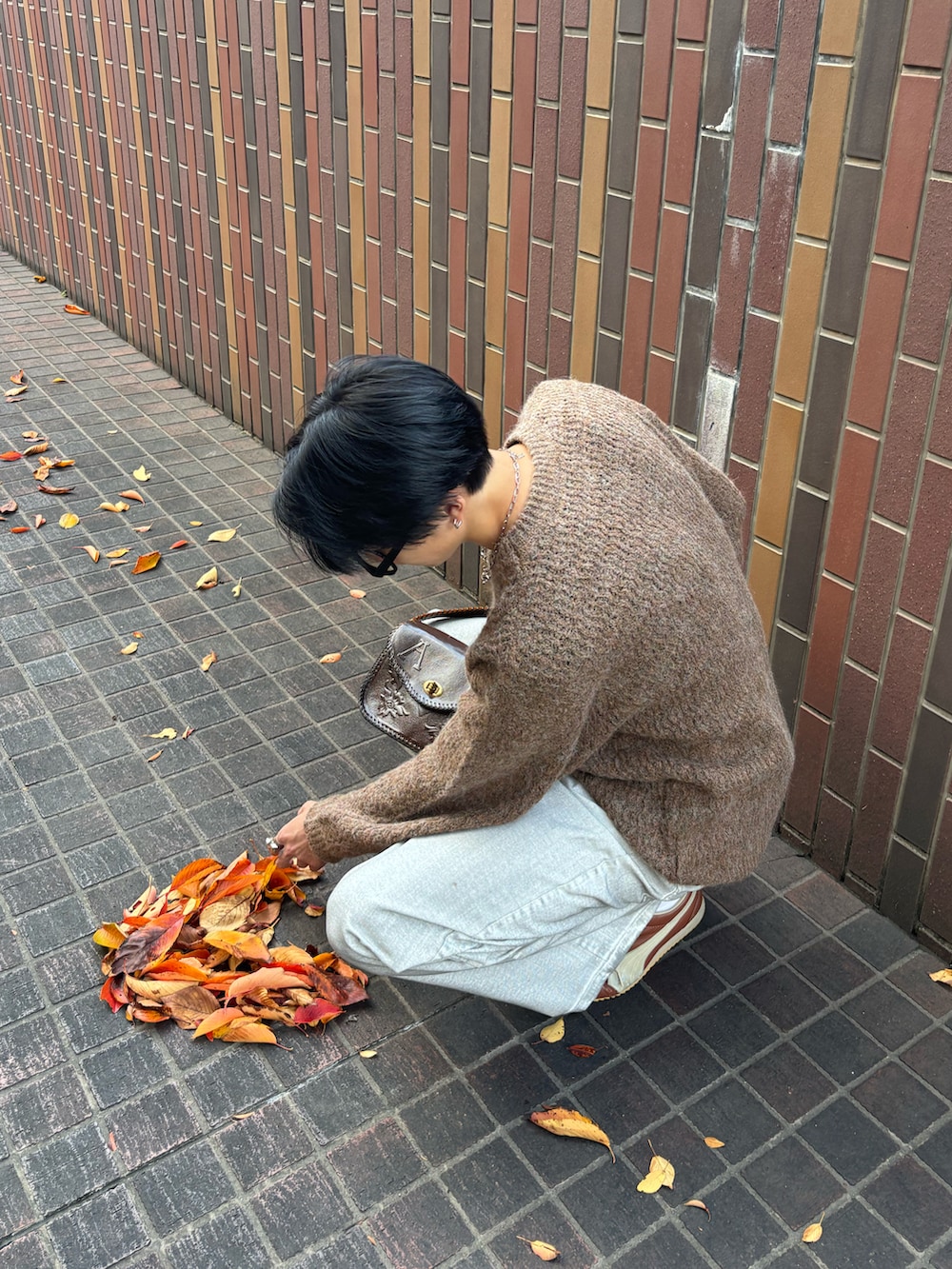 ブラウン系のニット/セーター、ホワイト系のデニムパンツ、ブラウン系のハンドバッグを着用したメンズの秋コーディネートの3枚目の写真