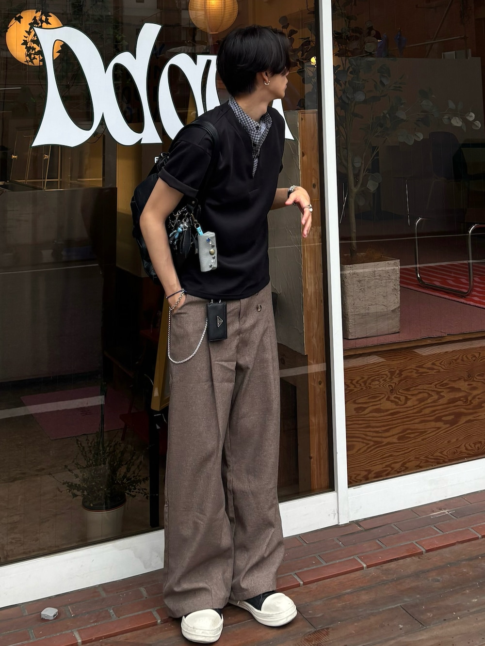 ブラック系のTシャツ/カットソー、ブラウン系のスラックス、ブラック系のスニーカーを着用したメンズの夏コーディネートの3枚目の写真