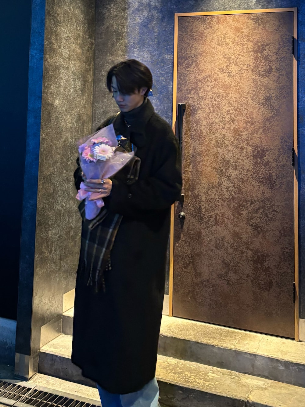 ブラック系のチェスターコート、グレー系のニット/セーター、ブルー系のデニムパンツを着用したメンズの冬コーディネートの2枚目の写真