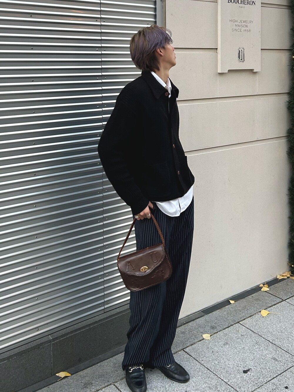 ブラック系のニット/セーター、ブラウン系のハンドバッグ、ブルー系のスラックスを着用したメンズの春コーディネートの2枚目の写真