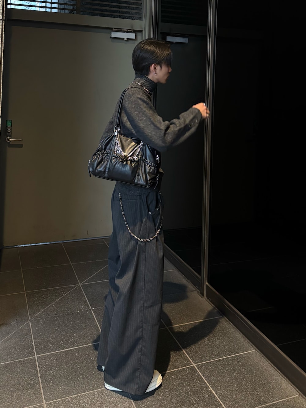 グレー系のニット/セーター、グレー系のスラックス、ブラック系のスニーカーを着用したメンズの冬コーディネートの2枚目の写真