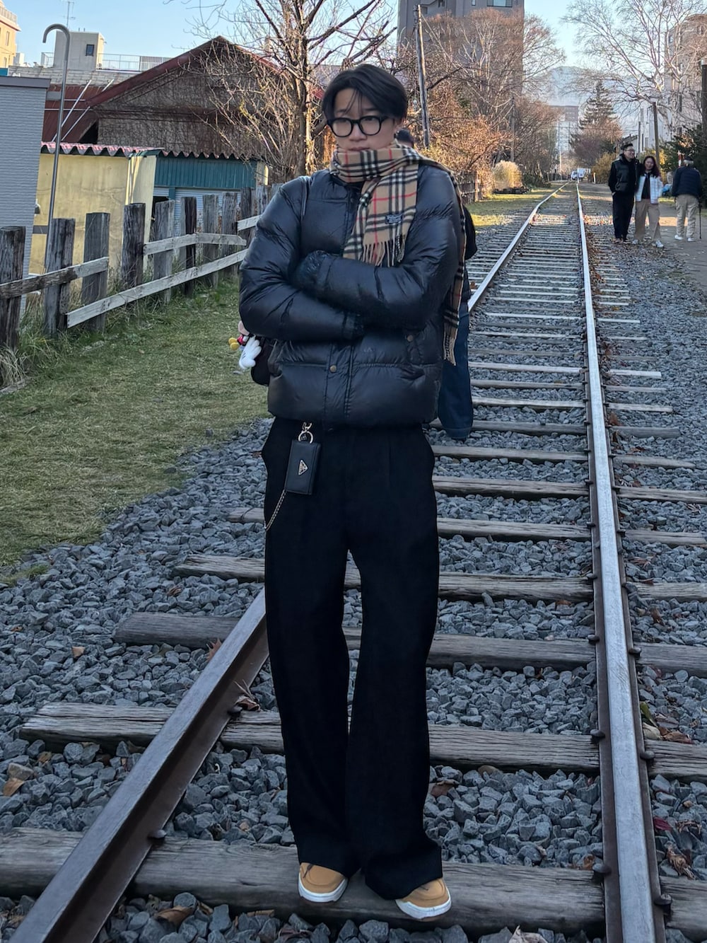 ブラウン系のショルダーバッグ、ブラック系のスラックス、イエロー系のスニーカーを着用したメンズの冬コーディネートの3枚目の写真