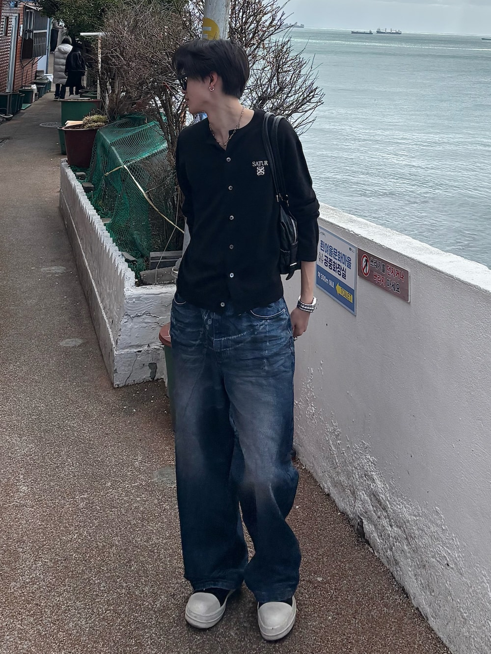 ブラック系のカーディガン/ボレロ、ブルー系のデニムパンツ、ブラック系のスニーカーを着用したメンズの冬コーディネートの2枚目の写真