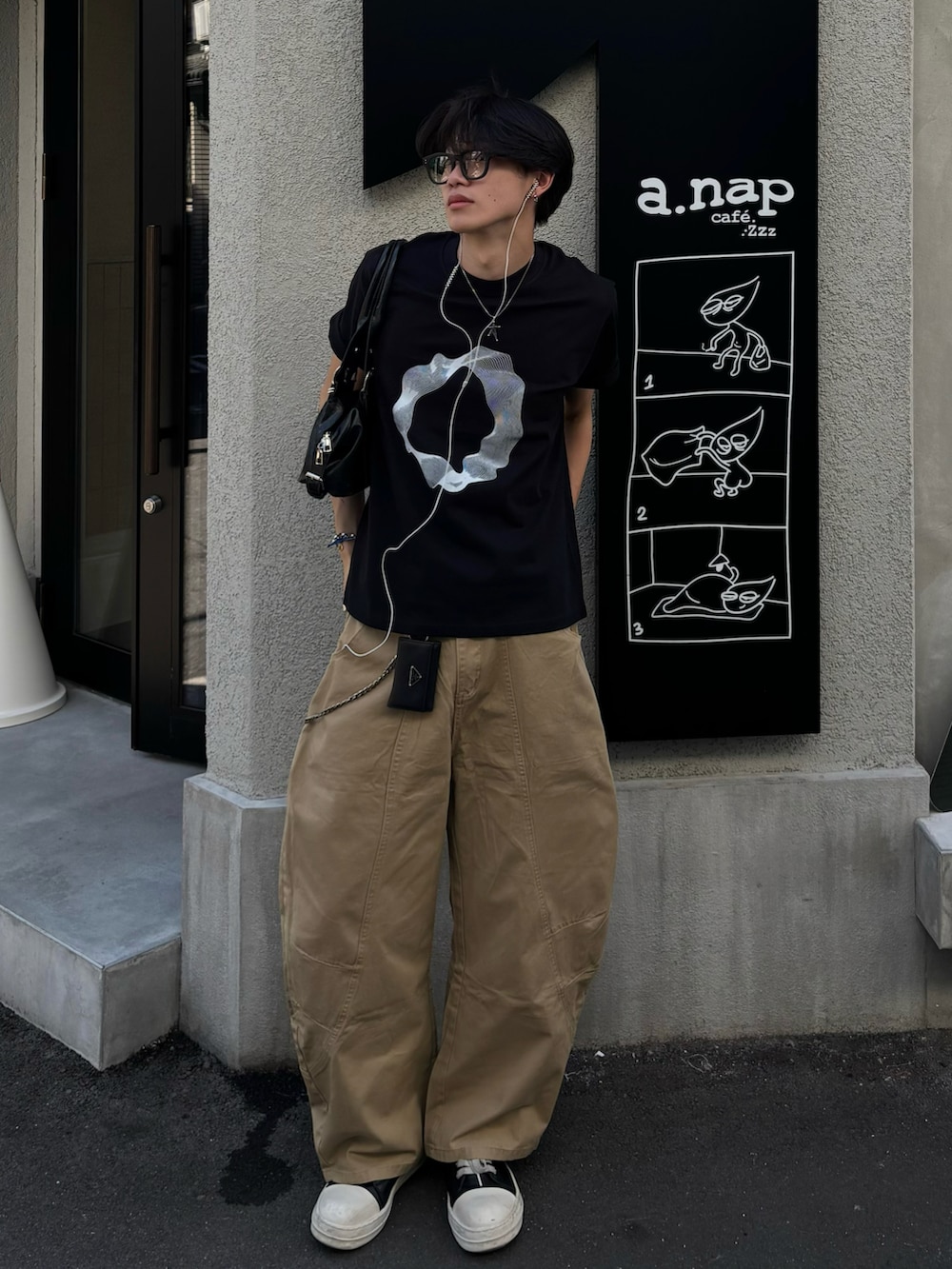 ブラック系のTシャツ/カットソー、ブラック系のショルダーバッグ、ベージュ系のチノパンツを着用したメンズの夏コーディネートの2枚目の写真