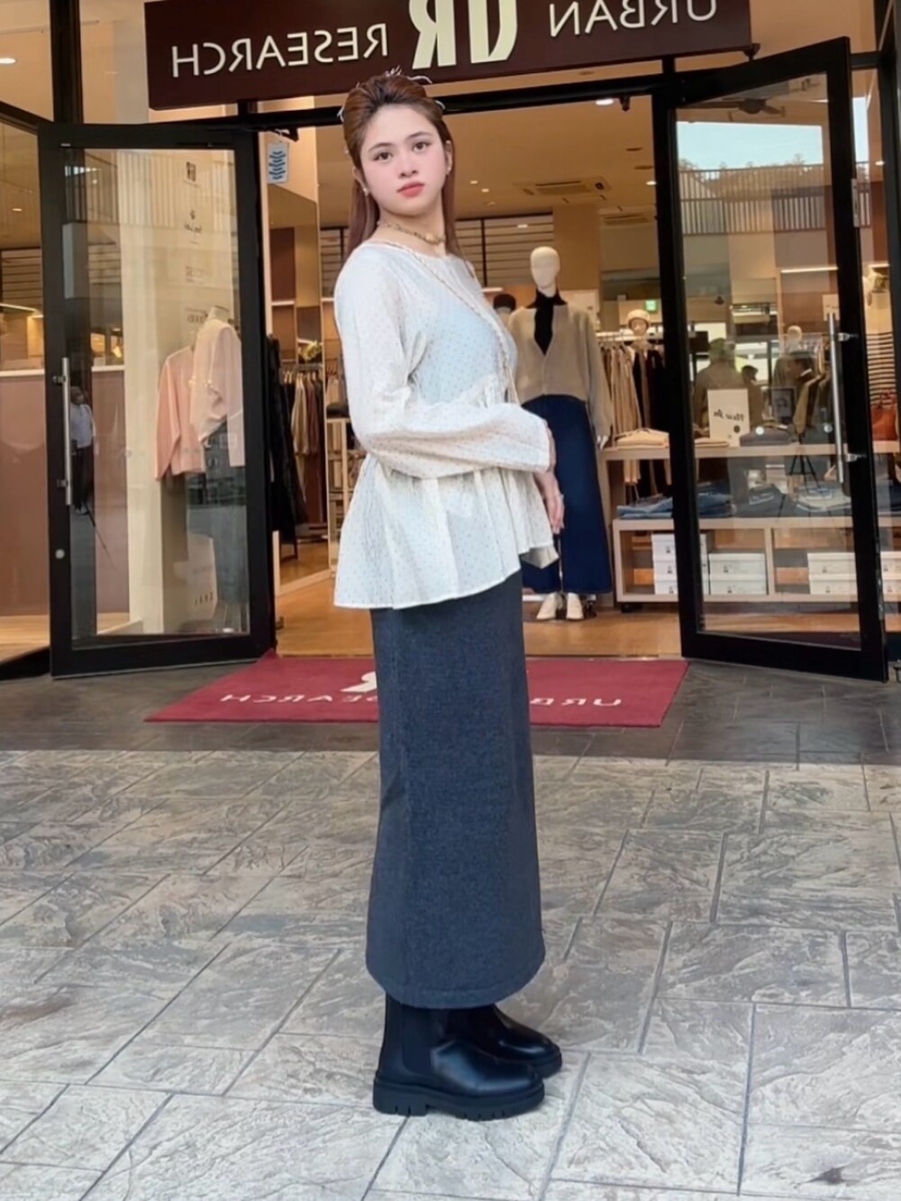 グレー系のスカート、ベージュ系のシャツ/ブラウス、ブラック系のブーツを着用したレディースの秋コーディネートの2枚目の写真