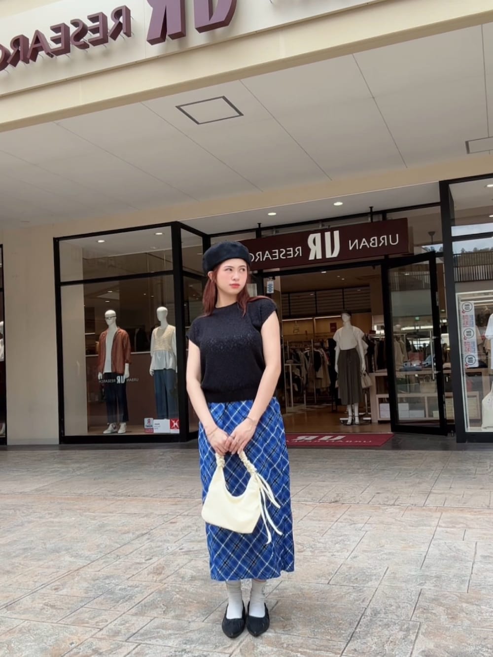 ブラック系のベスト、ブルー系のスカート、ホワイト系のハンドバッグを着用したレディースの秋コーディネートの4枚目の写真