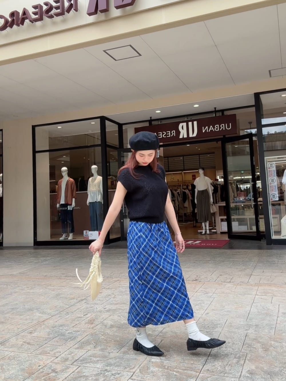 ブラック系のベスト、ブルー系のスカート、ホワイト系のハンドバッグを着用したレディースの秋コーディネートの3枚目の写真