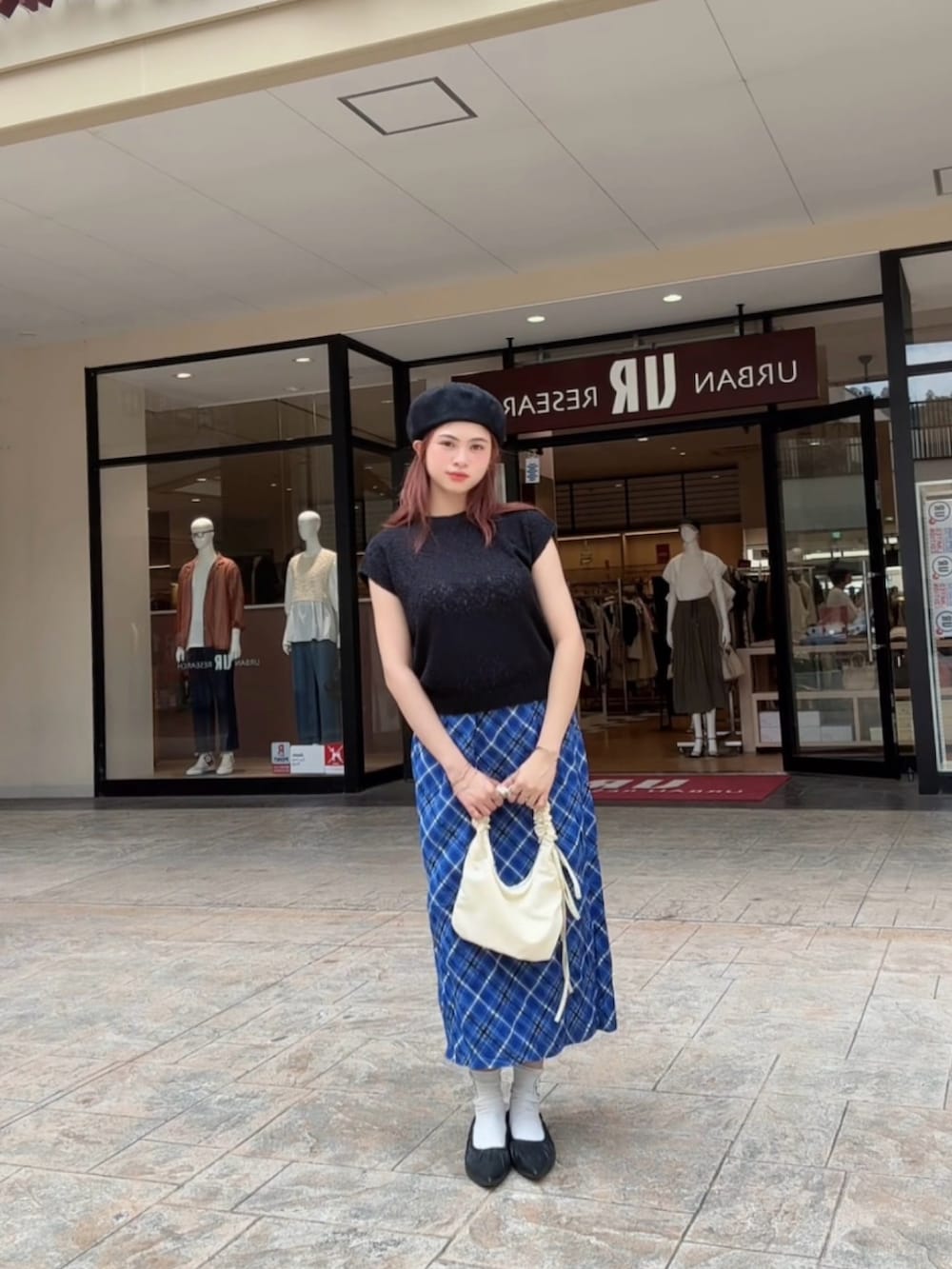 ブラック系のベスト、ブルー系のスカート、ホワイト系のハンドバッグを着用したレディースの秋コーディネートの2枚目の写真