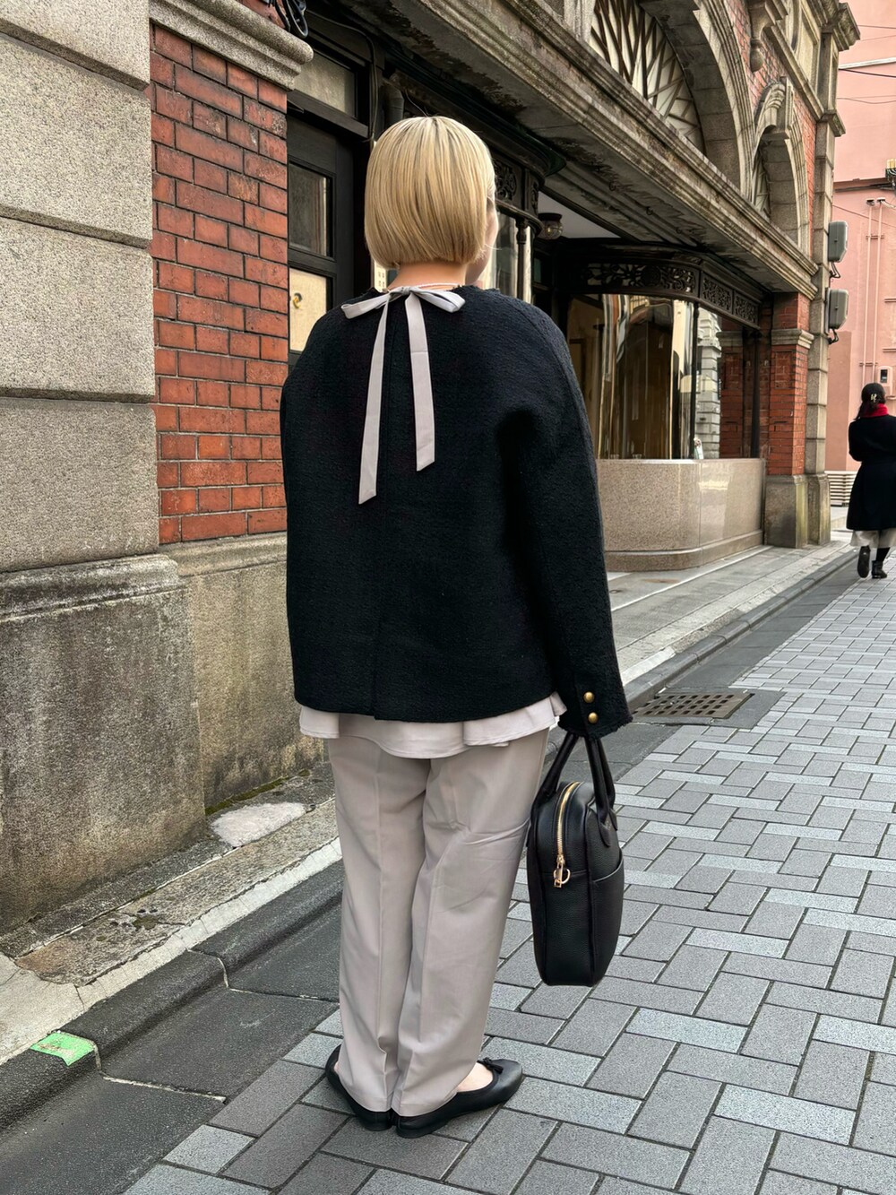 ブラック系のハンドバッグ、ブラック系のノーカラージャケット、ベージュ系のパンツを着用したレディースの冬コーディネートの3枚目の写真