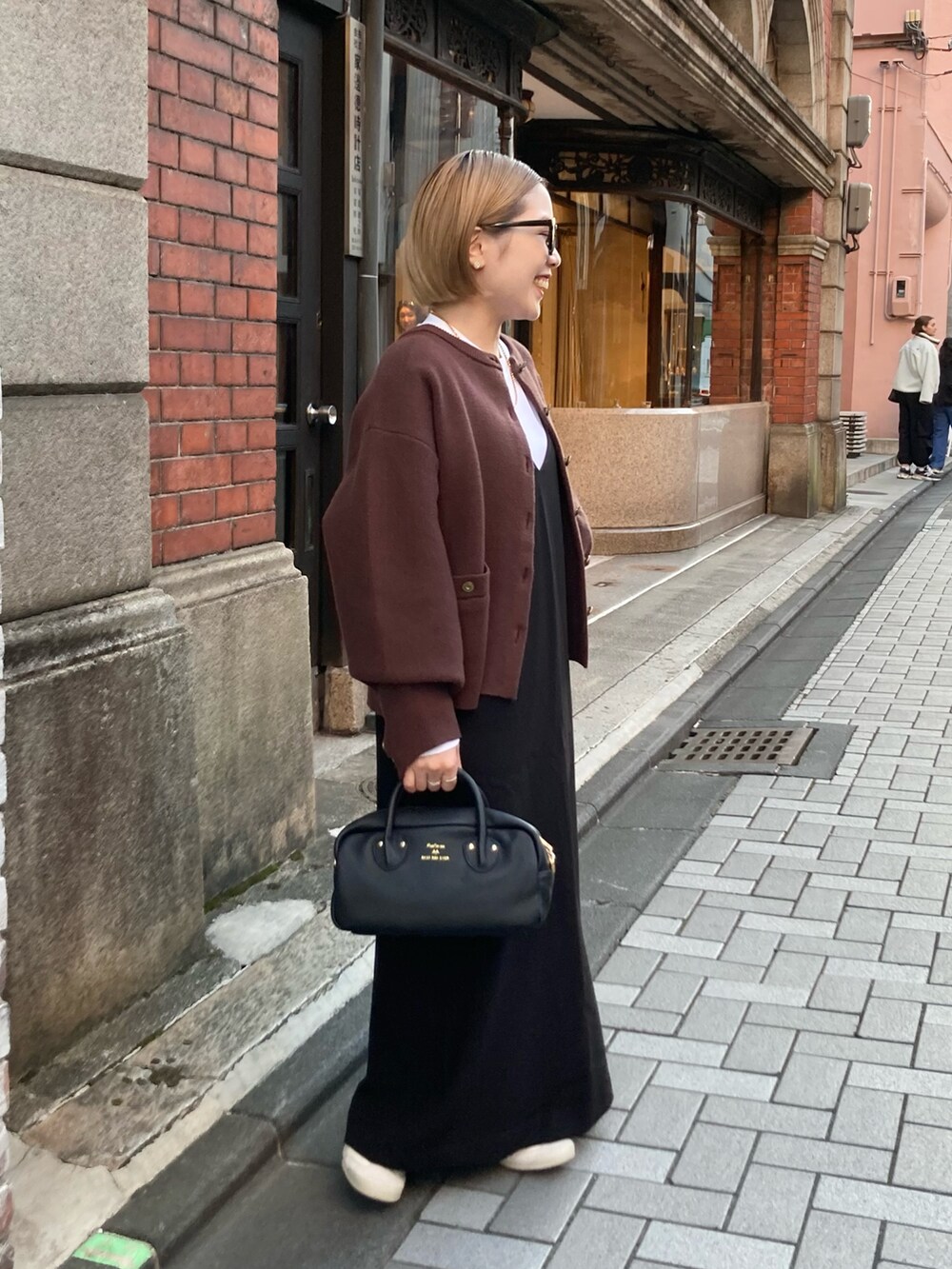 ブラック系のショルダーバッグ、ブラウン系のカーディガン/ボレロ、ブラック系のワンピースを着用したレディースの秋コーディネートの3枚目の写真