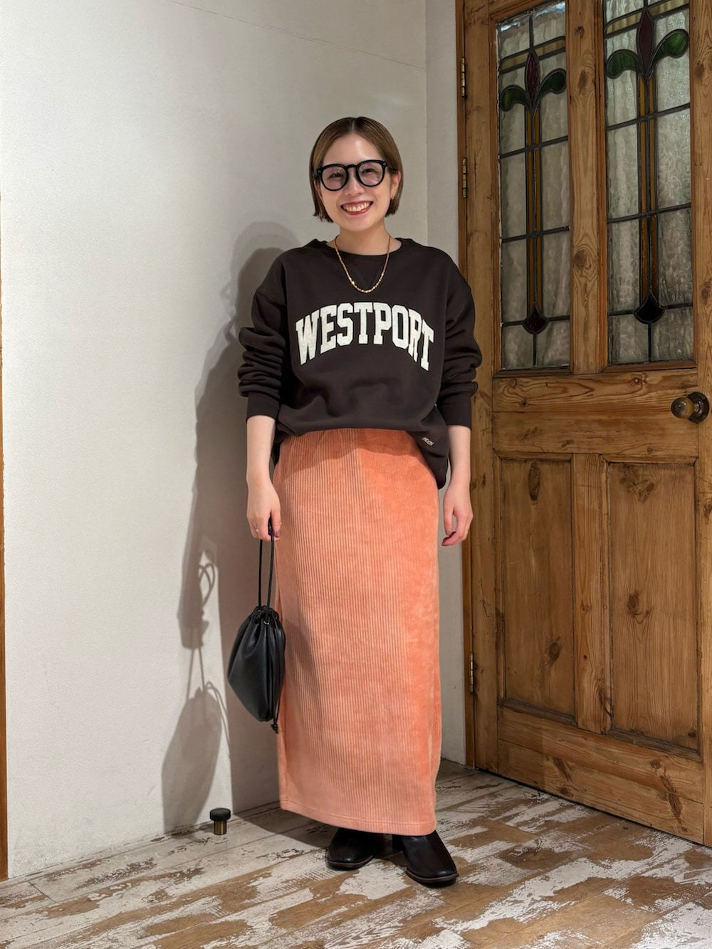 ピンク系のスカート、ブラック系のショルダーバッグ、ブラック系のブーツを着用したレディースの秋コーディネートの4枚目の写真