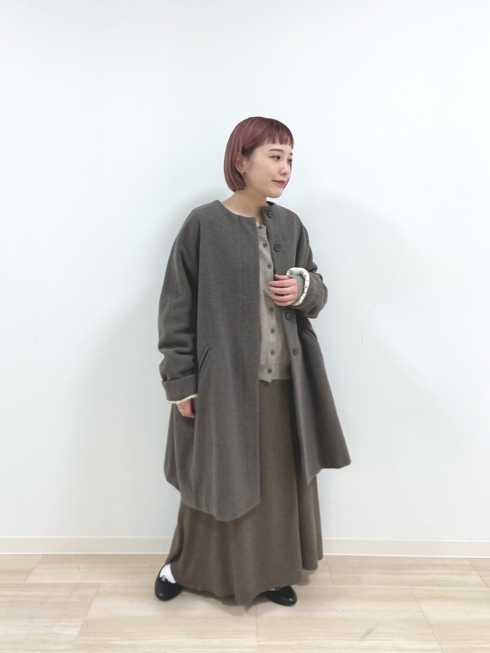 ブラウン系のノーカラーコート、ベージュ系のニット/セーター、ブラウン系のスカートを着用したレディースの冬コーディネートの4枚目の写真