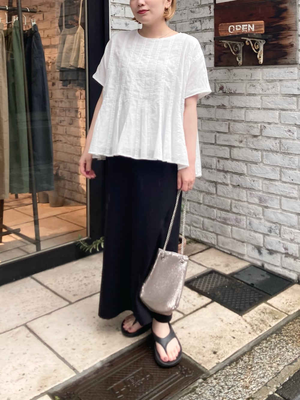 ホワイト系のシャツ/ブラウス、ブラック系のスカート、ブラック系のサンダルを着用したレディースの夏コーディネートの3枚目の写真