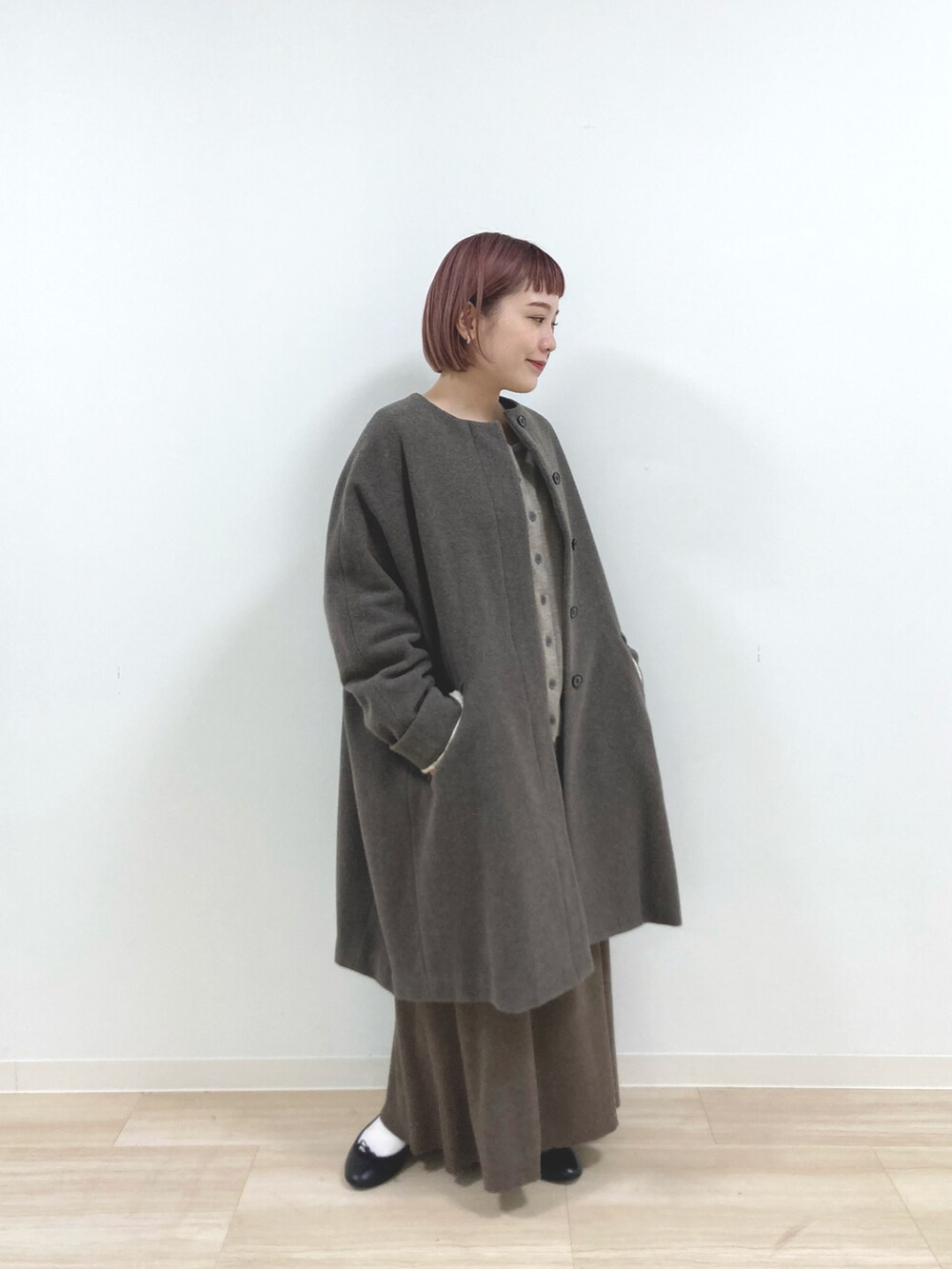 ブラウン系のノーカラーコート、ベージュ系のニット/セーター、ブラウン系のスカートを着用したレディースの冬コーディネートの3枚目の写真