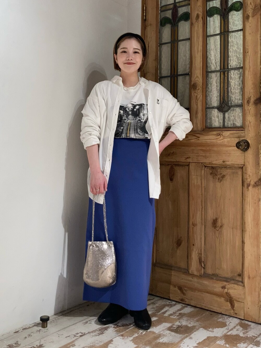 ブラック系のブーツ、ゴールド系のショルダーバッグ、ブルー系のスカートを着用したレディースの春コーディネートの2枚目の写真