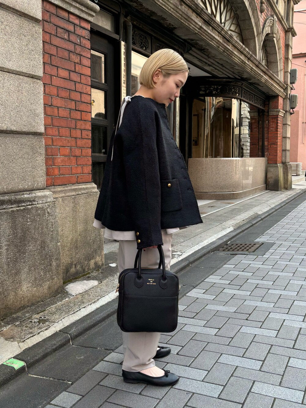 ブラック系のハンドバッグ、ブラック系のノーカラージャケット、ベージュ系のパンツを着用したレディースの冬コーディネートの2枚目の写真